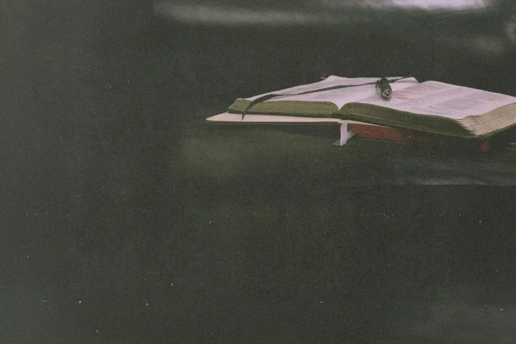 Close-up of an open Bible with a ribbon marker and reading glasses placed on top, set against a dark background