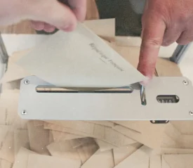 A hand places an envelope into a metal ballot box slot, with many sealed envelopes already collected inside