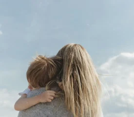 Blonde woman hugging young boy with blue sky background