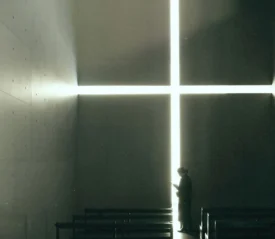 Person standing in between pews and a bright light that forms a tall thin cross