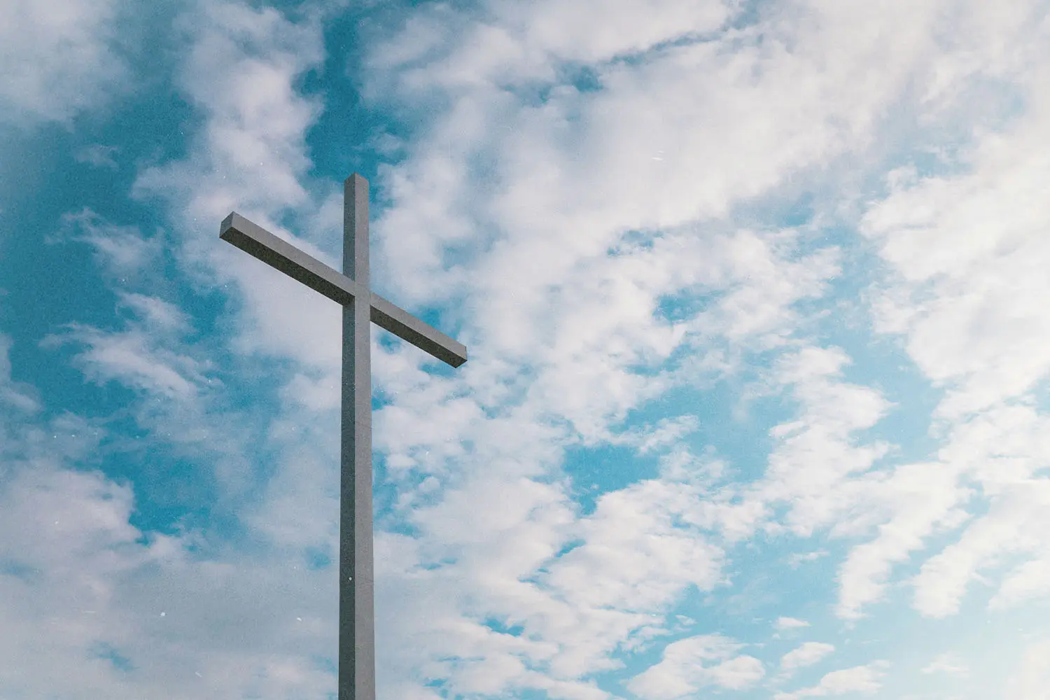Large metal cross standing against a bright sky filled with scattered white clouds