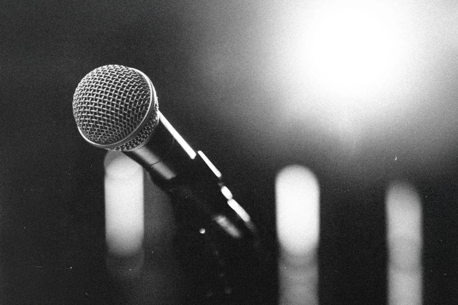 Close-up of a microphone on a stand with bright stage lights glowing in the background