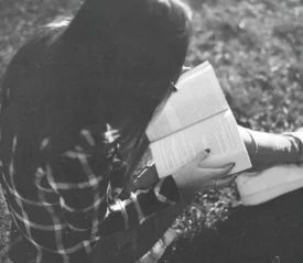 Person sitting on grass outdoors, holding an open book while reading in soft natural light
