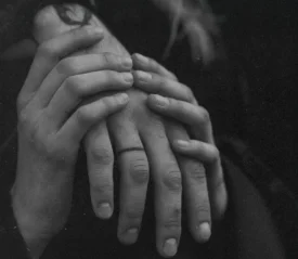 Close‑up of two people gently holding hands in a black‑and‑white scene