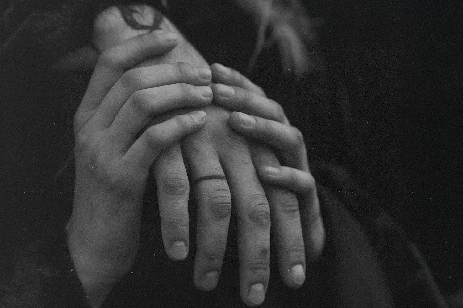 Close‑up of two people gently holding hands in a black‑and‑white scene