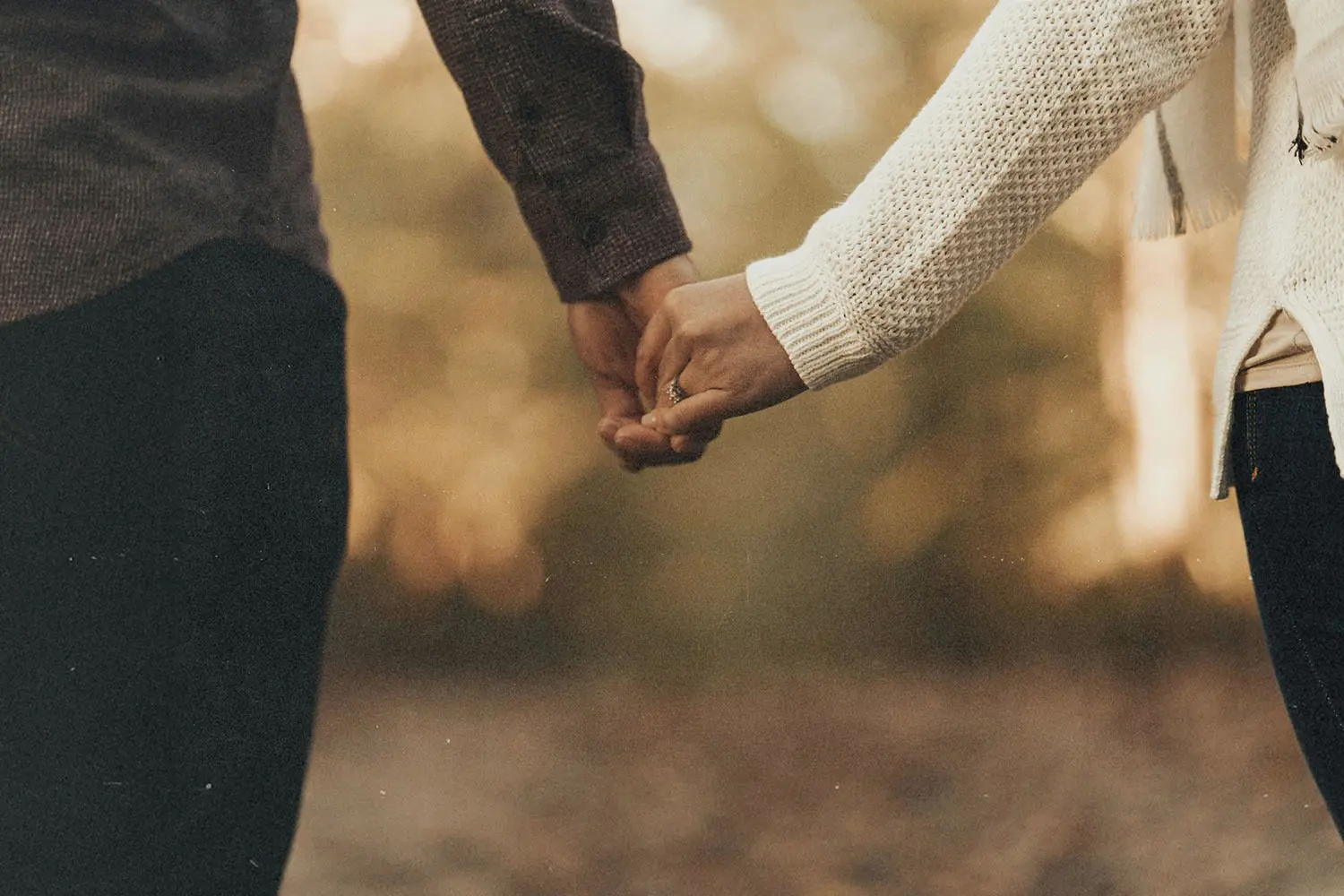 Two people holding hands outdoors with warm, soft sunlight in the background