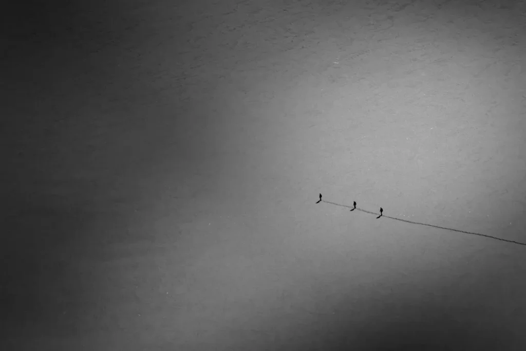 Line of 3 people walking, following the same line in the sand