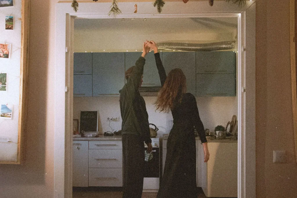 Two people dance together in a warmly lit kitchen, holding hands as they spin between the doorway and the counter