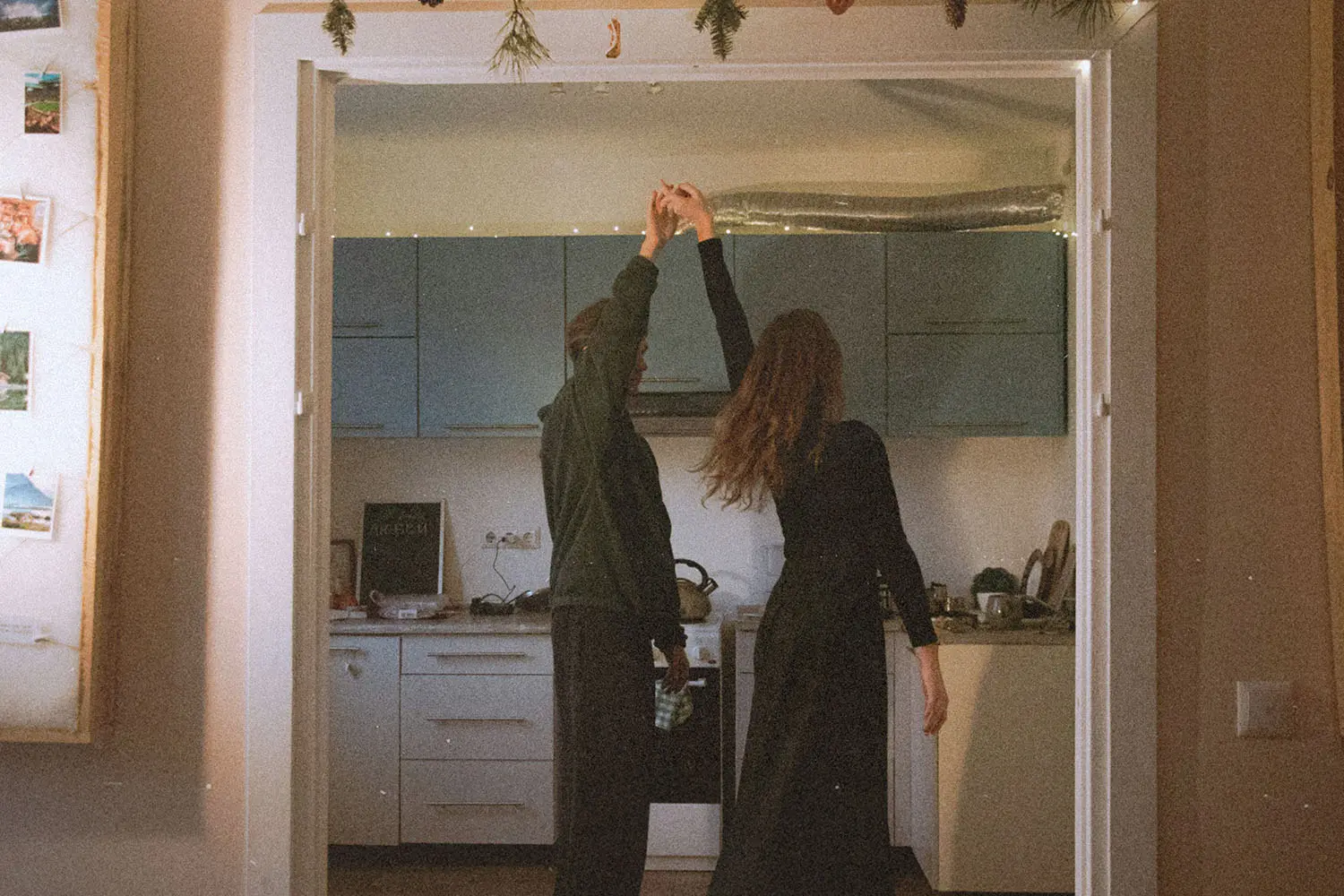 Two people dance together in a warmly lit kitchen, holding hands as they spin between the doorway and the counter