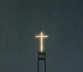 Illuminated cross glowing against a dark night sky atop a tall church structure