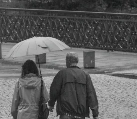 man and woman walking with an umbrella in a park like setting