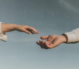 Two outstretched hands reaching toward each other against a soft blue sky, as if about to connect