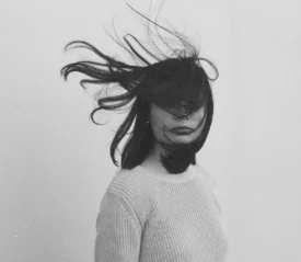 Person facing forward with their hair blowing in their face