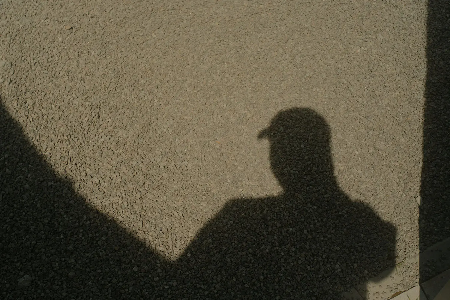 shadow of a person wearing a hat on gravel