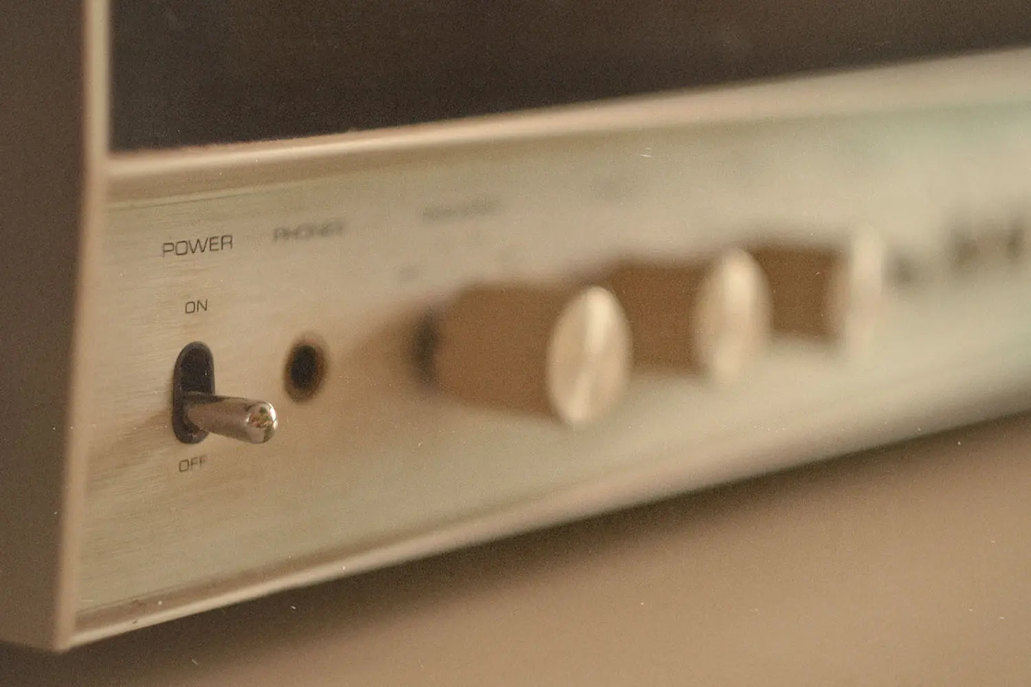 Close-up of a vintage audio receiver showing a metal power toggle switch and several blurred control knobs
