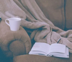 book open on a chair with a mug and a blanket