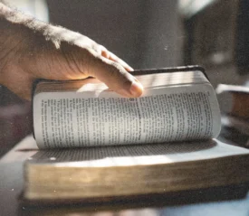 Hand turning a page in an open Bible as sunlight shines across the text