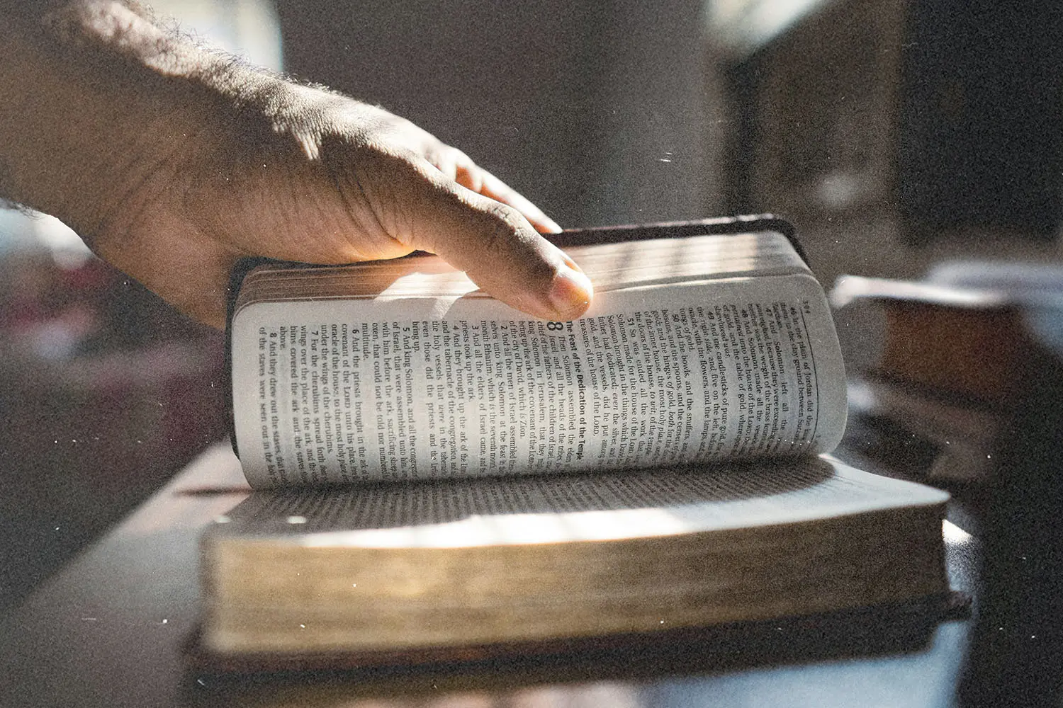 Hand turning a page in an open Bible as sunlight shines across the text