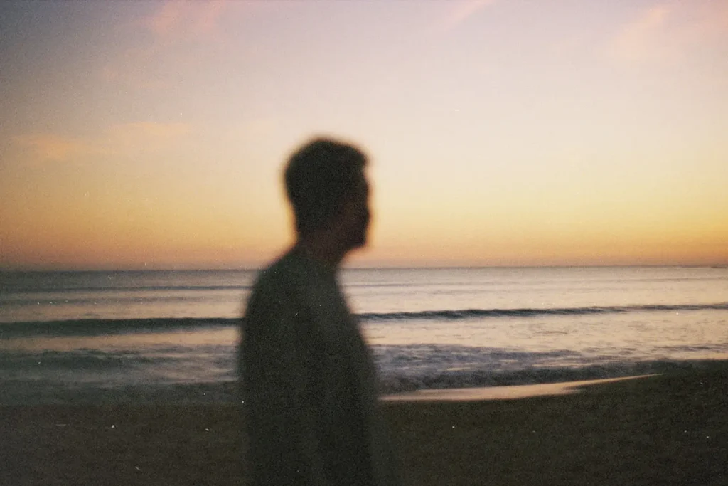 Silhouetted figure standing on the beach at sunset with gentle waves rolling onto the shore