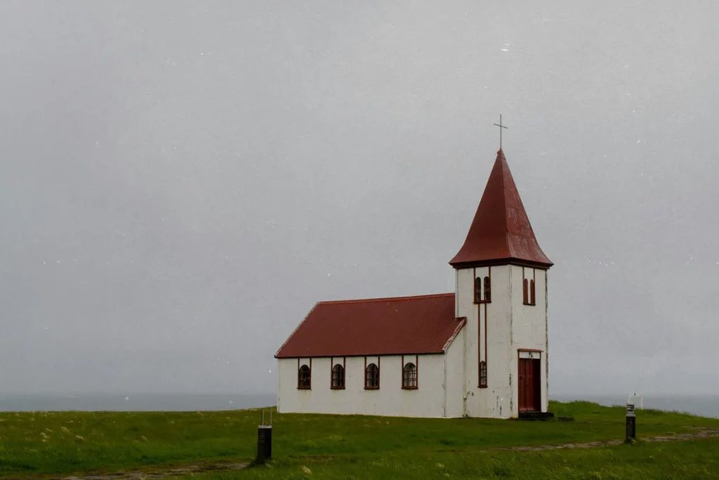 older white church with red roof in the middle of a field