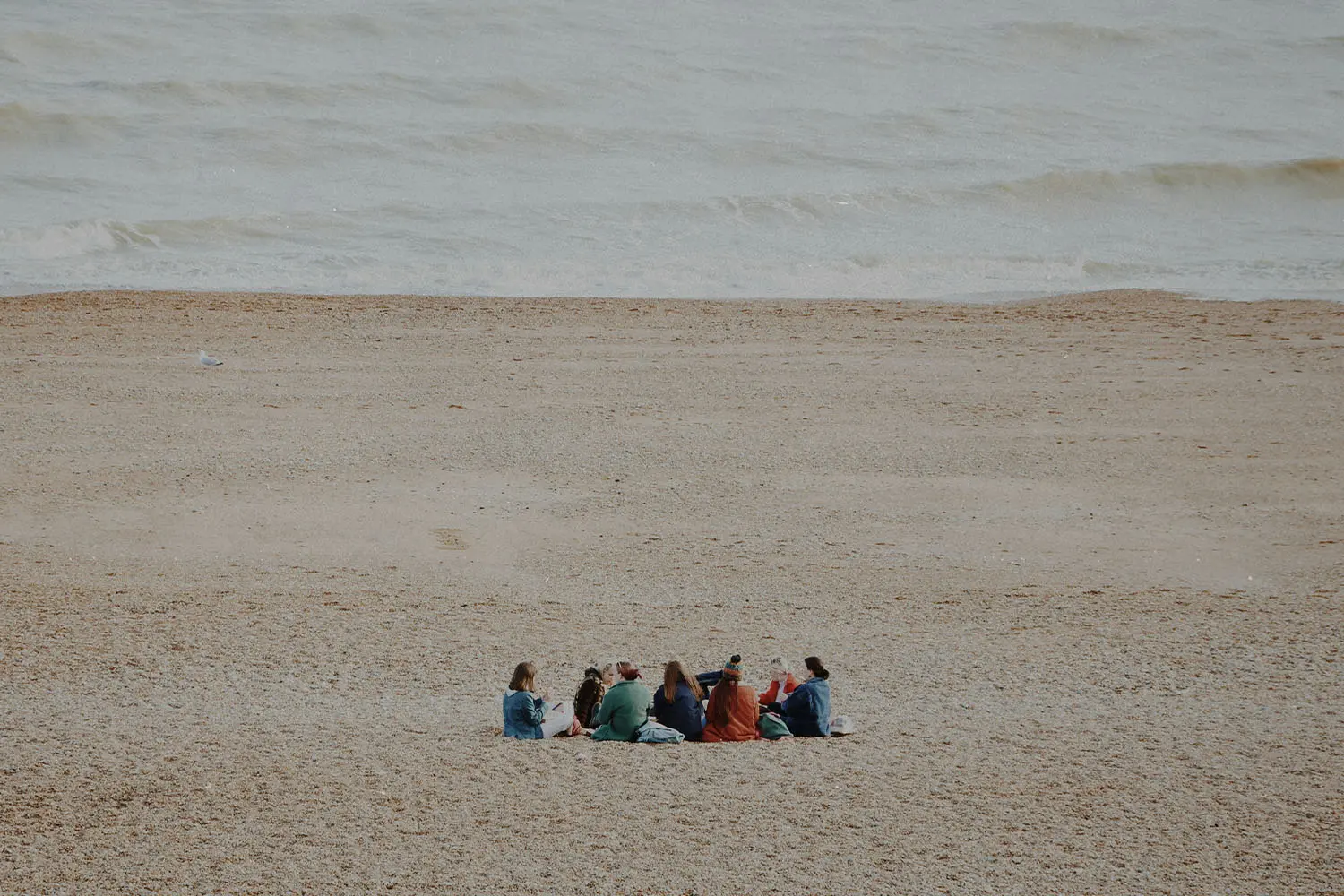 Friends gathered in a circle on a sandy beach near gentle ocean waves