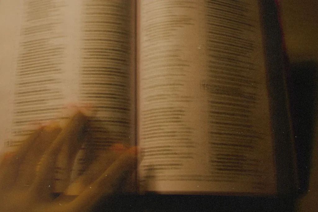 A blurred close‑up of an open Bible with a hand gliding across the page, softly lit in warm tones