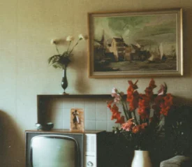 Vintage living room with an old television, floral arrangements, and a framed painting hanging above a tiled fireplace