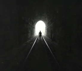 Man walking on train tracks in a tunnel towards light