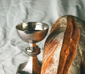 Silver communion cup filled with wine beside a loaf of rustic bread on a soft fabric background