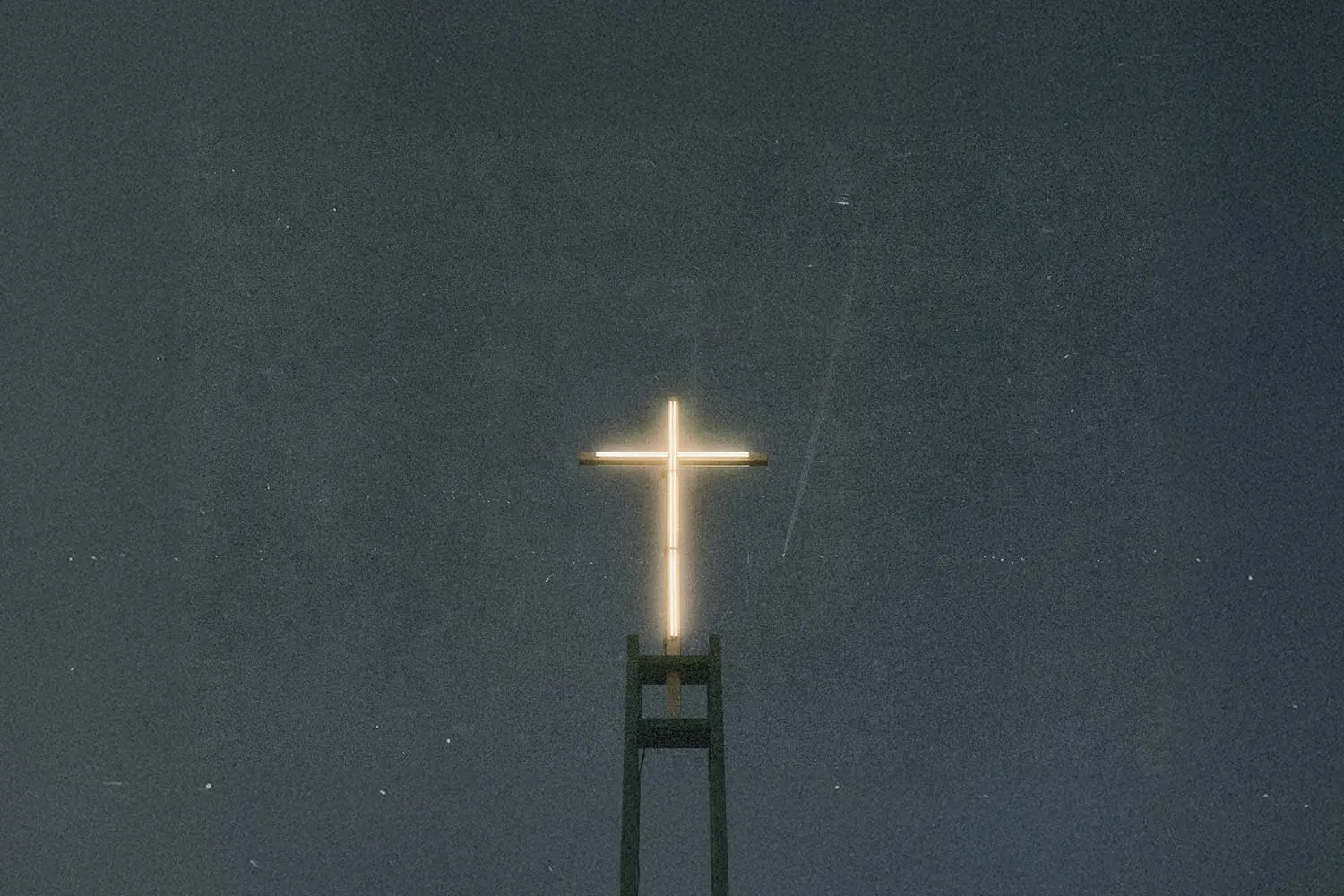 A glowing cross sits atop a tall structure against a dark, starless night sky