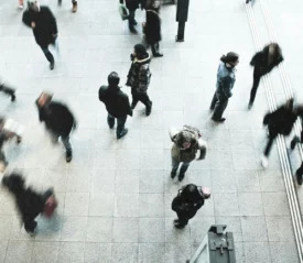 A busy indoor walkway filled with people in motion, seen from above with blurred movement showing the rush of foot traffic