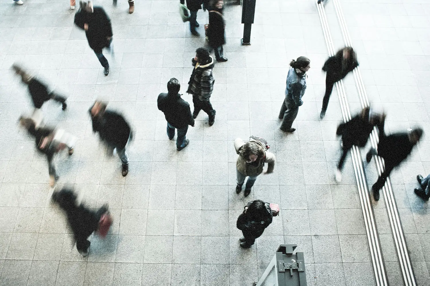 A busy indoor walkway filled with people in motion, seen from above with blurred movement showing the rush of foot traffic