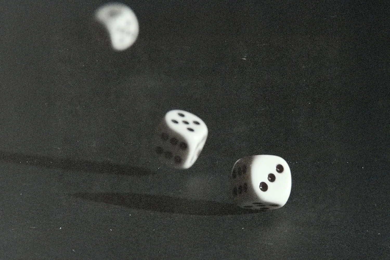 Three white dice captured midair and on a dark surface, frozen in motion as they tumble during a roll