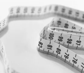 A coiled measuring tape lies on a smooth surface, with black numbers and markings visible along its length