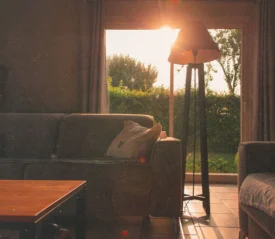 Warm sunlight streams through a large window into a cozy living room with sofas and a floor lamp