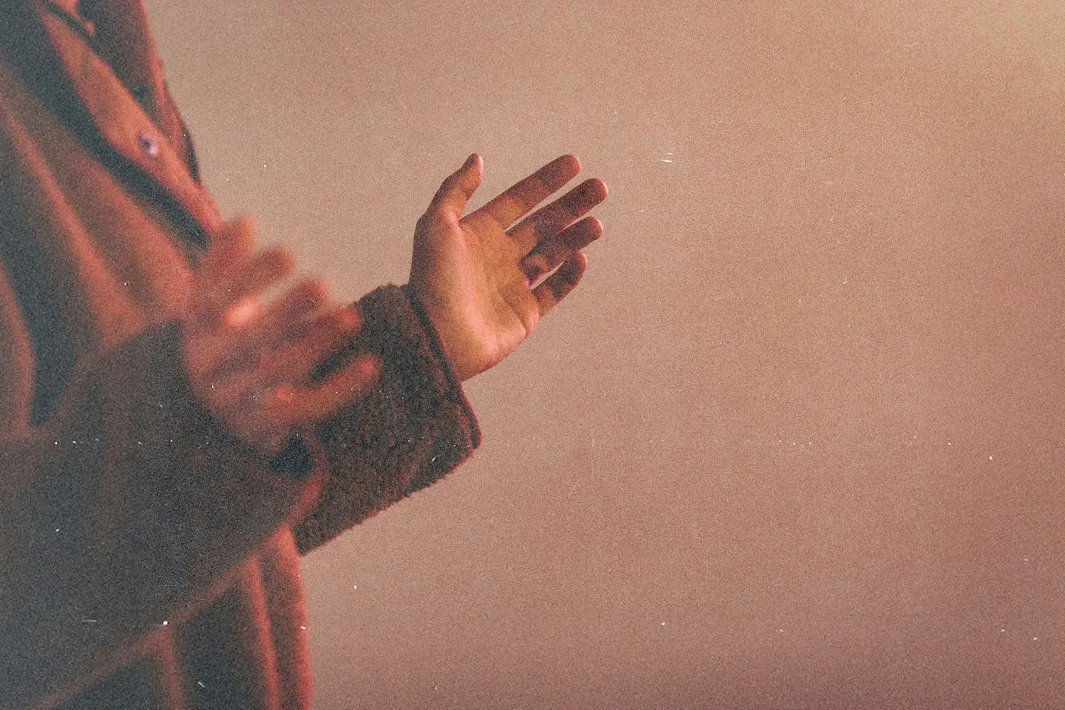 Hands raised slightly upward against a warm-toned background, suggesting prayer