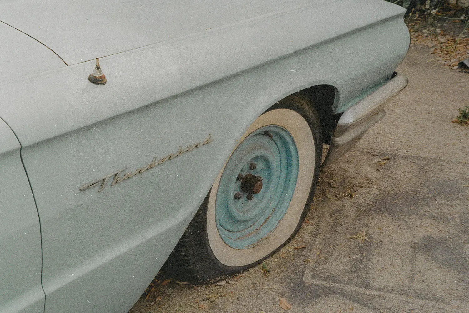Close-up of a vintage car’s rear wheel and fender parked along a concrete curb