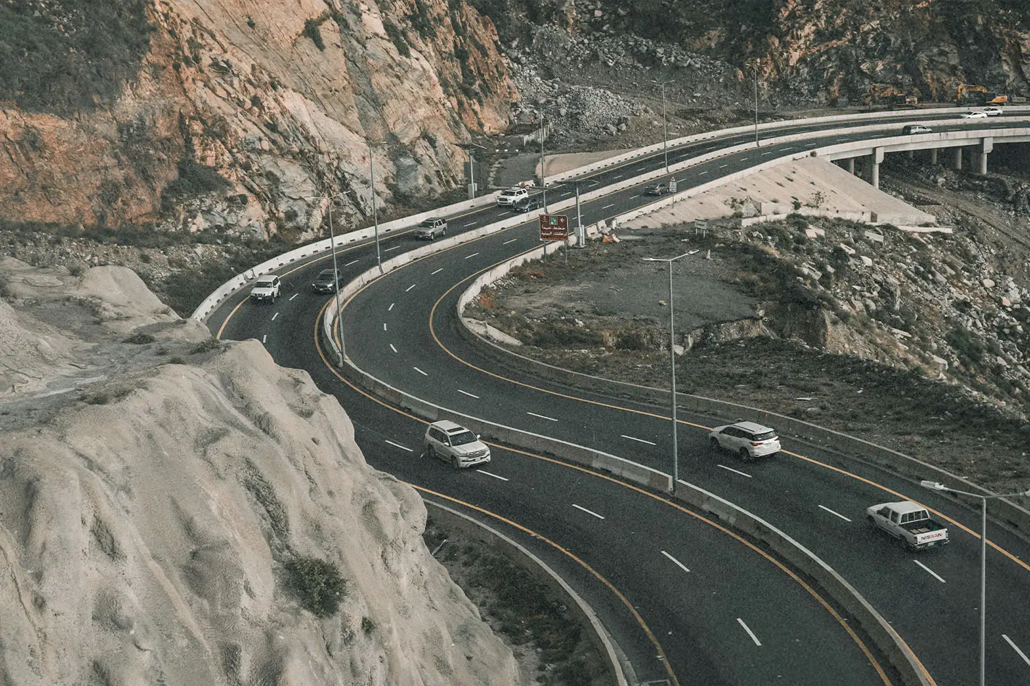 curved road with cars driving. Bolders on one side and a drop off on the other