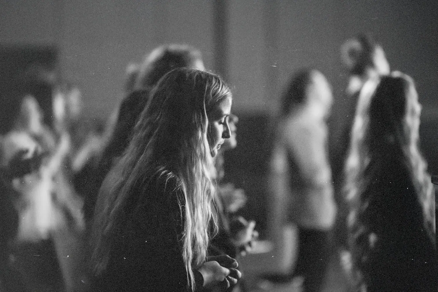 Group of people standing closely together in a dimly lit indoor setting during worship.