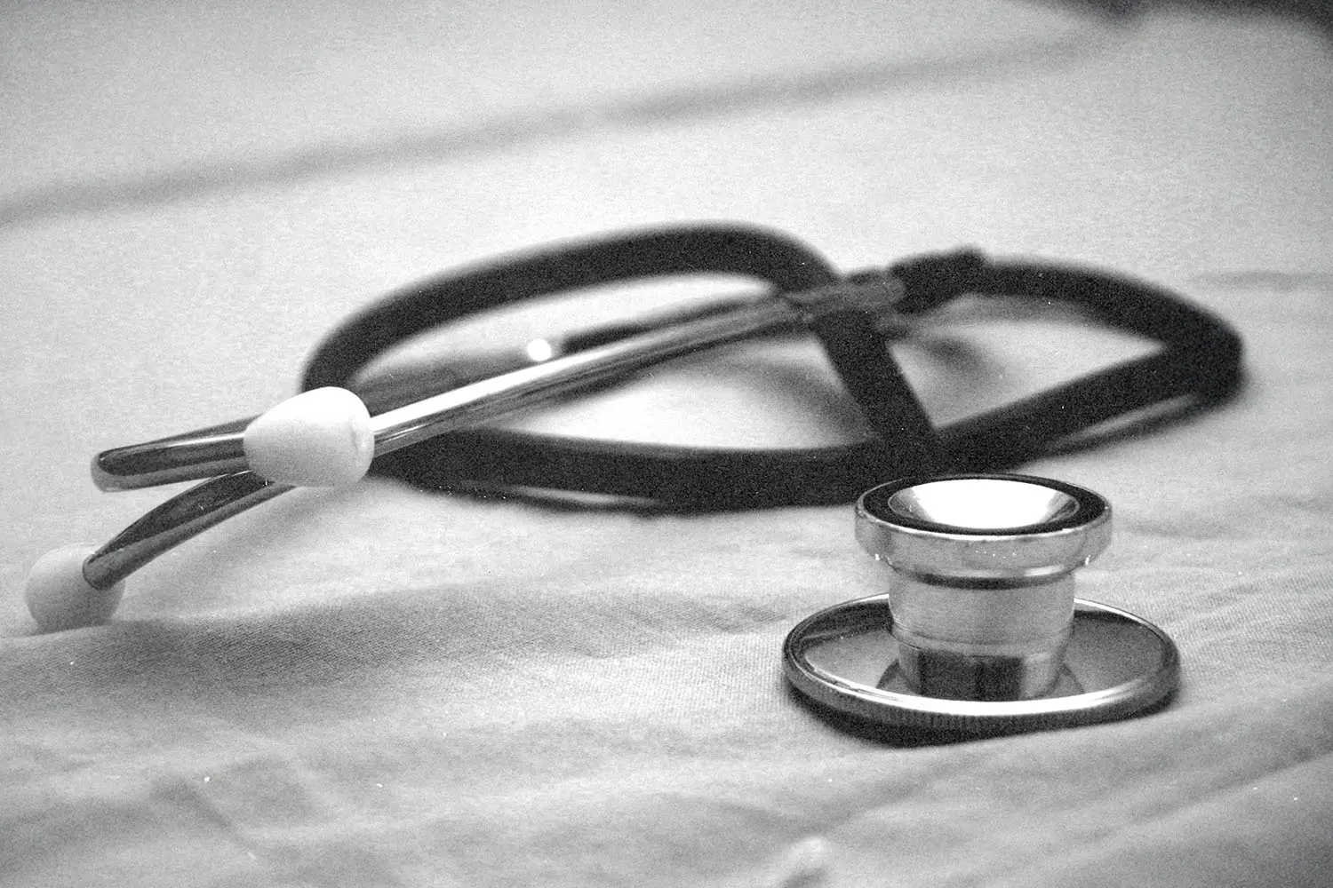 Stethoscope resting on a fabric surface in a softly lit black‑and‑white setting