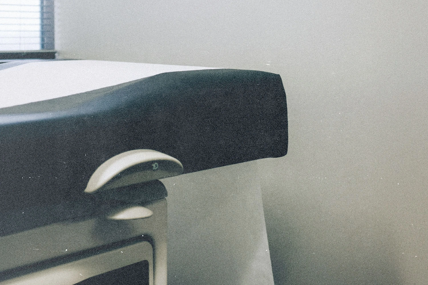 Close-up of a padded black armrest attached to a medical examination table inside a softly lit room with light-colored walls