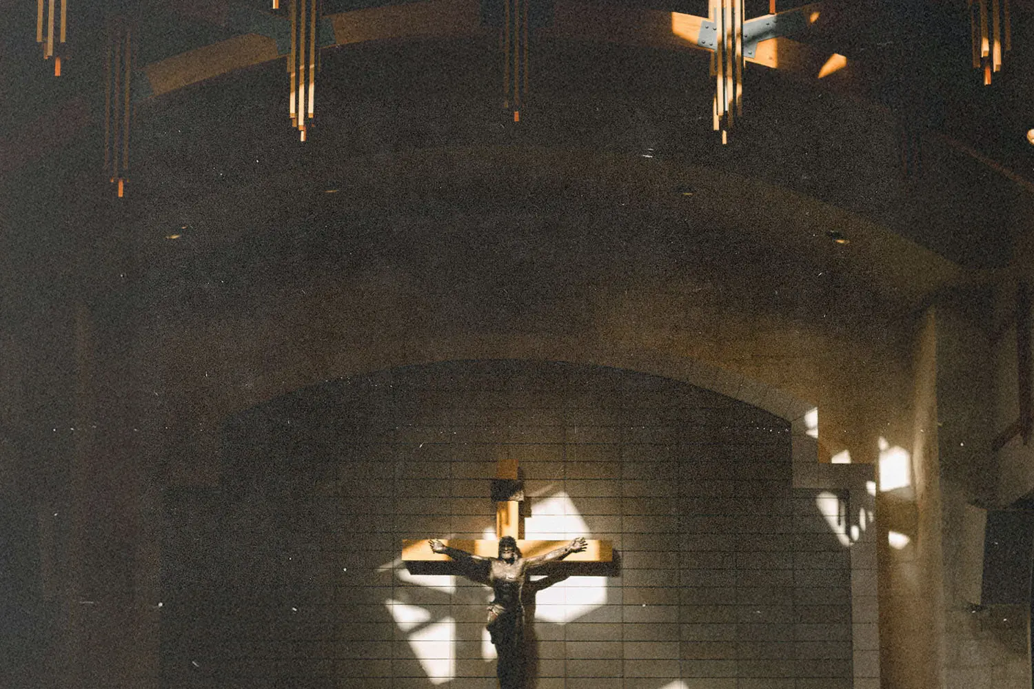 Interior of a church with a large cross and a crucifix illuminated by soft light beneath a high wooden ceiling