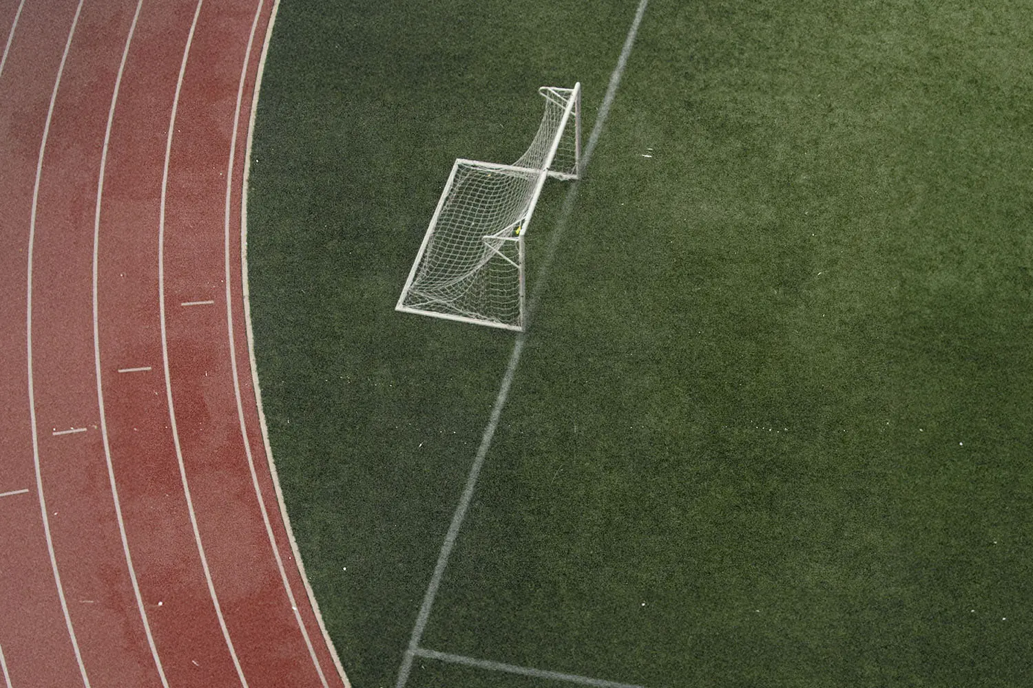 An aerial view of a soccer goal on a green field beside a red running track