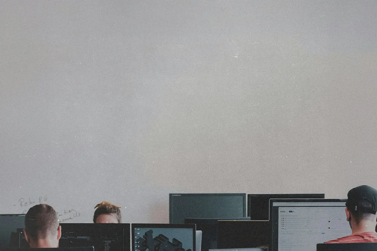 People seated at computer stations in a classroom with multiple monitors facing the front of the room
