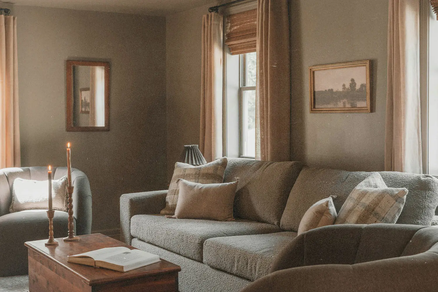 Warm living room with sofas, candles, framed wall art, and a wooden coffee table near softly lit windows