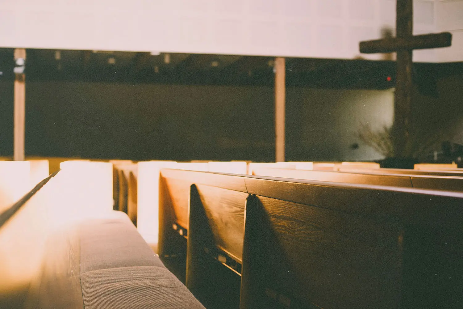 Sunlight illuminating wooden church pews with a large wooden cross visible at the front