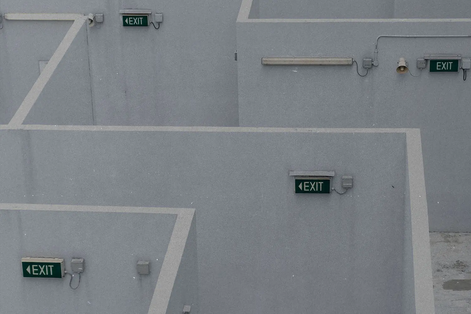 Series of concrete walls forming a maze-like structure with green illuminated exit signs mounted throughout