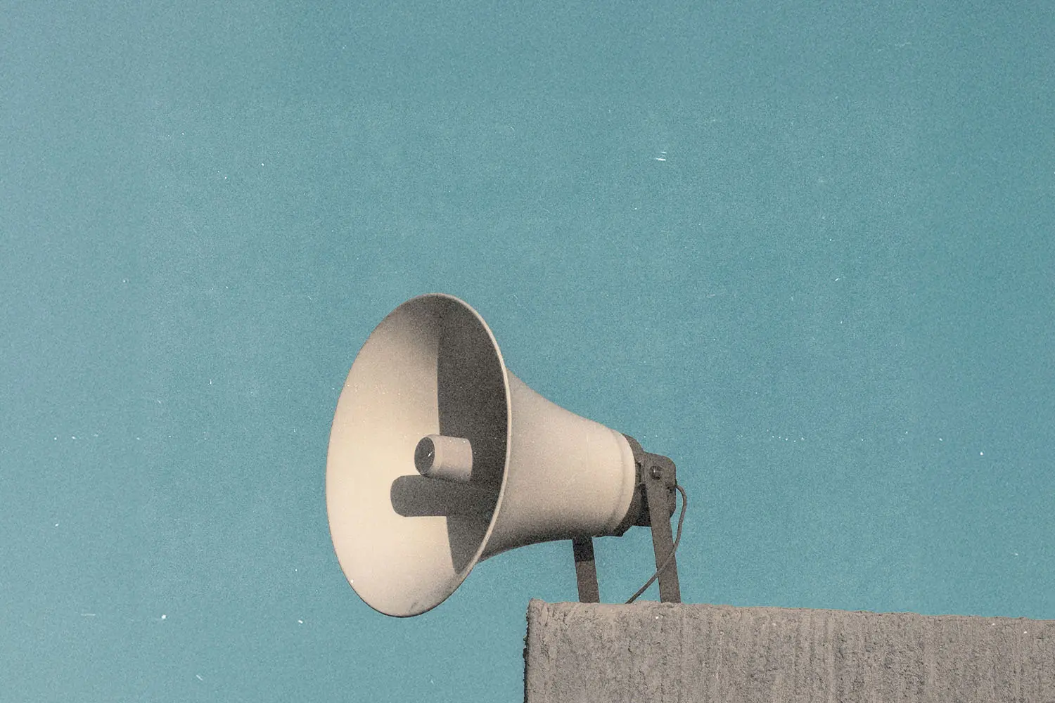 Wall-mounted outdoor loudspeaker facing upward against a clear blue sky