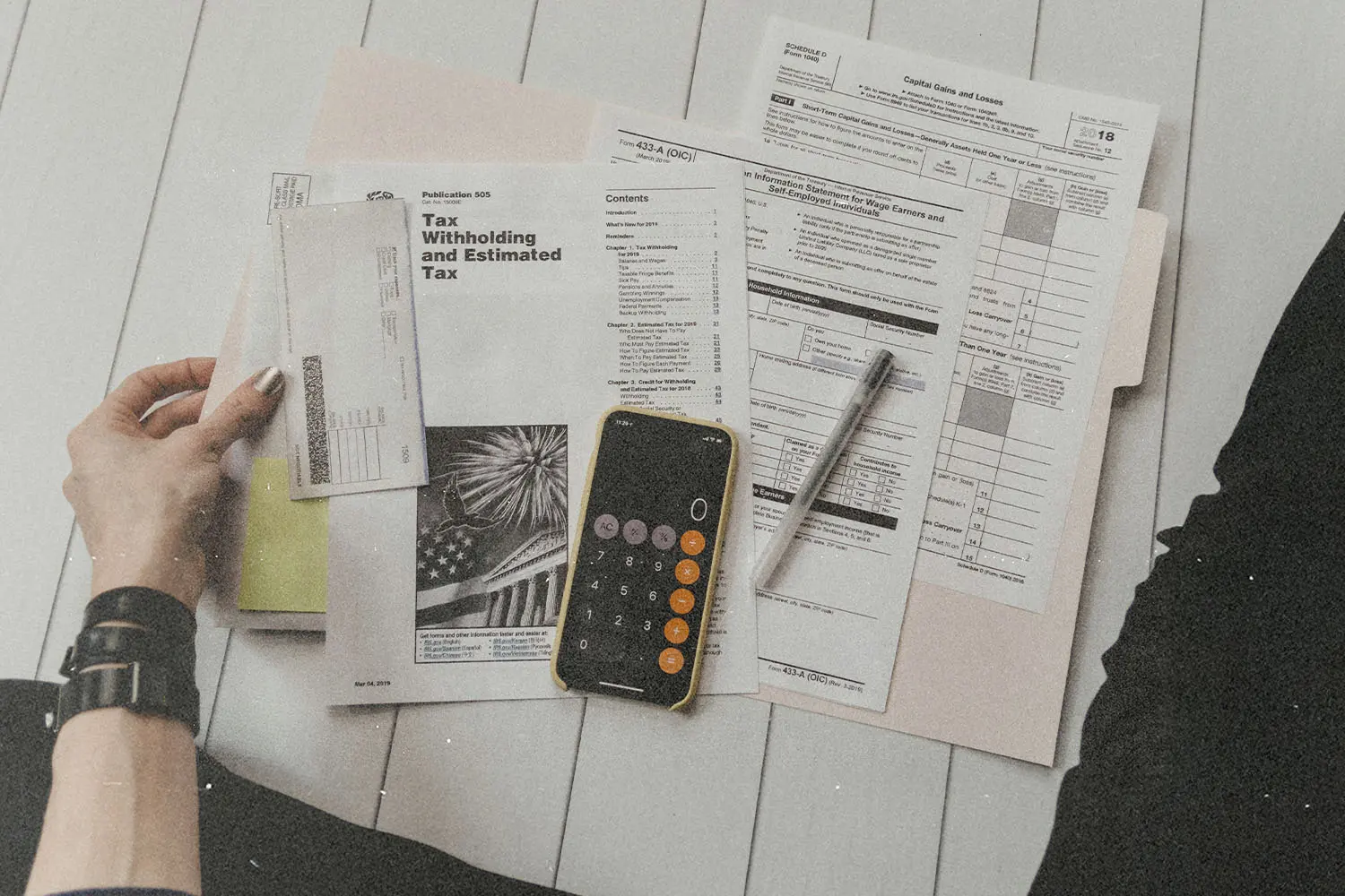 Assorted tax forms and financial papers spread out beside a smartphone calculator and pen