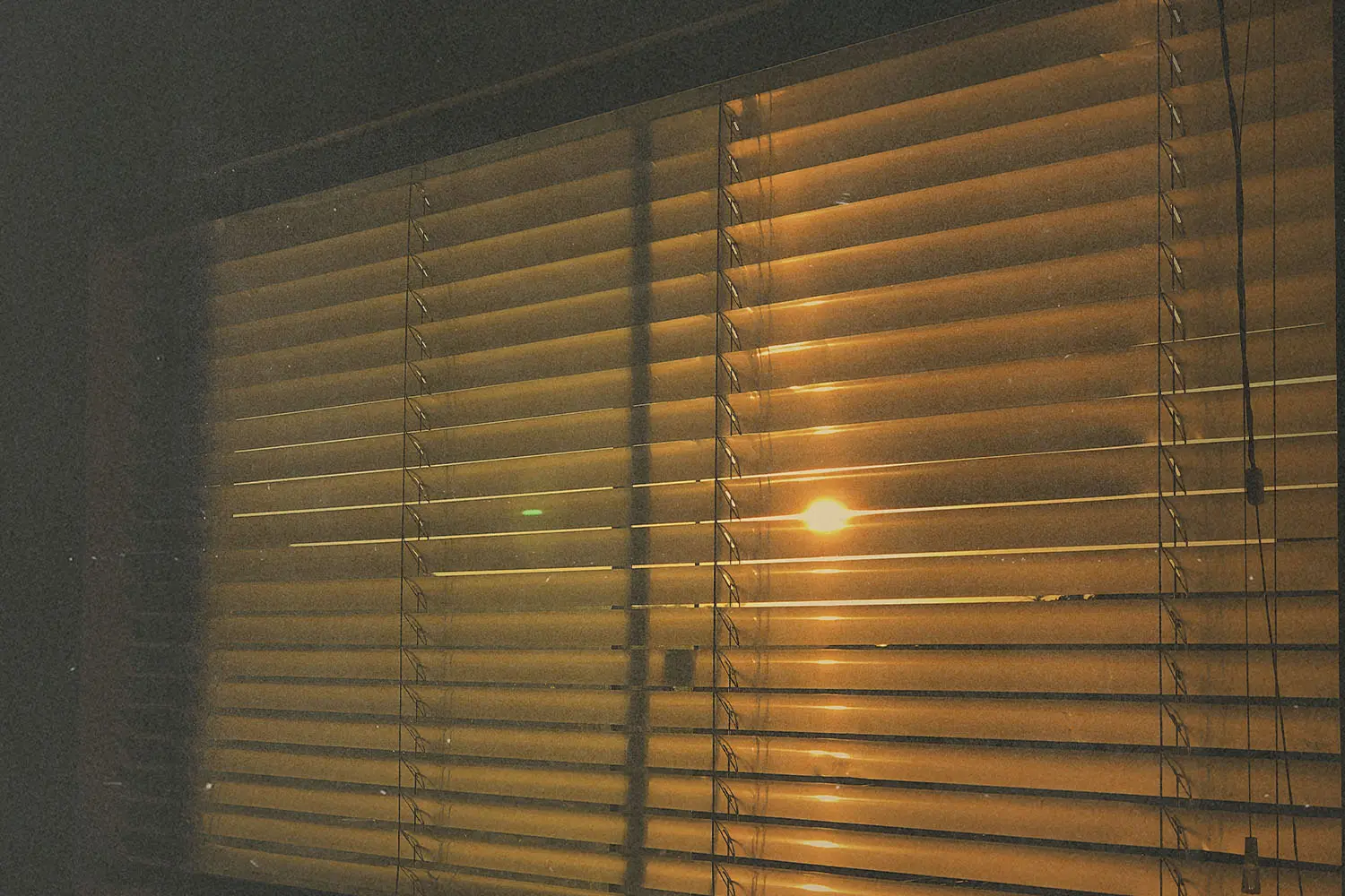 Warm sunlight shining through partially closed window blinds in a dark room